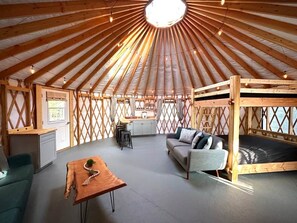 Et teltindretning med hvælvet træloft, sofa, spiseplads og køjeseng.