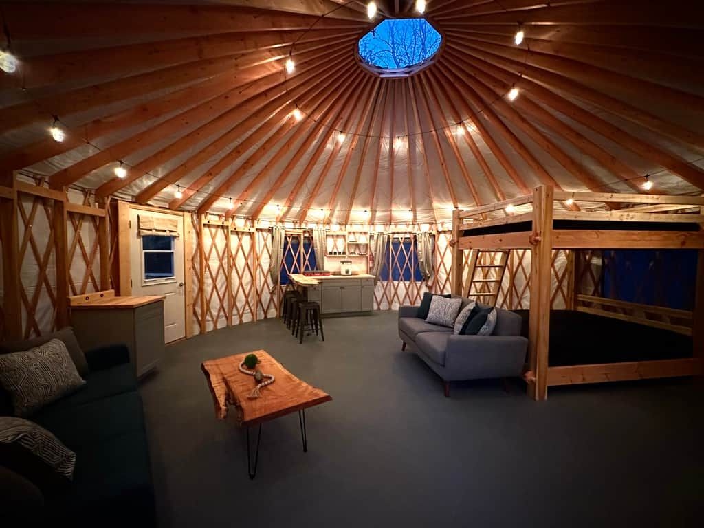 A yurt interior with a central seating area, a kitchenette, and a sleeping area.