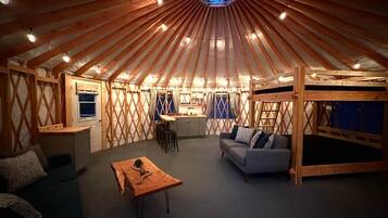 A yurt interior with a central seating area, a kitchenette, and a sleeping area.
