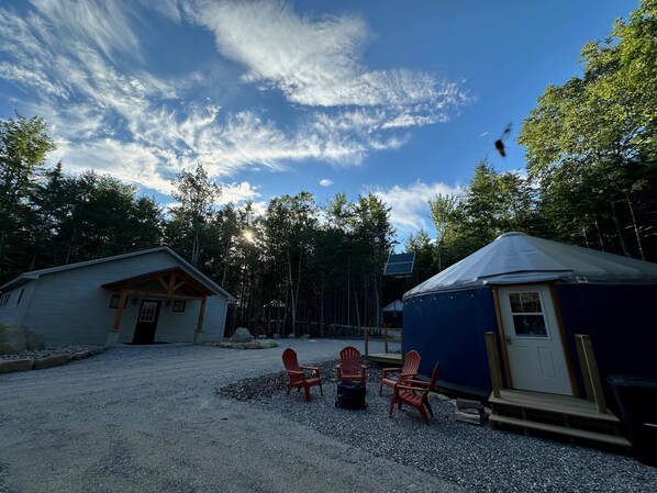 A cabin with a gravel driveway, a small shed, and a blue tent-like structure.