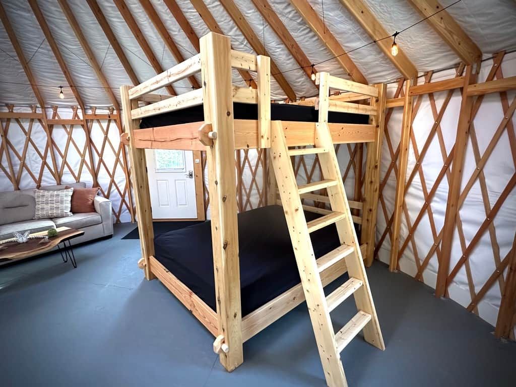 A wooden bunk bed with a ladder in a room with a high ceiling and a lattice wall.