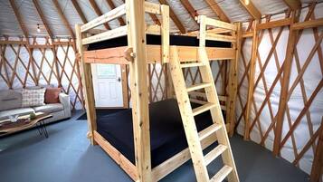 A wooden bunk bed with a ladder in a room with a high ceiling and a lattice wall.