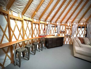 Un alojamiento en tienda de campaña con estructura interior de madera, una zona de bar con taburetes y un sofá.
