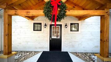 A wooden exterior with a black door, a red bow on a wreath, and a concrete pathway leading to the door.