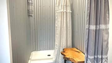 A small bathroom with a shower, a wooden stool, and a towel rack.