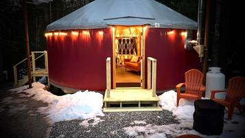 A yurt with a warm interior light, a wooden entrance, and outdoor seating.