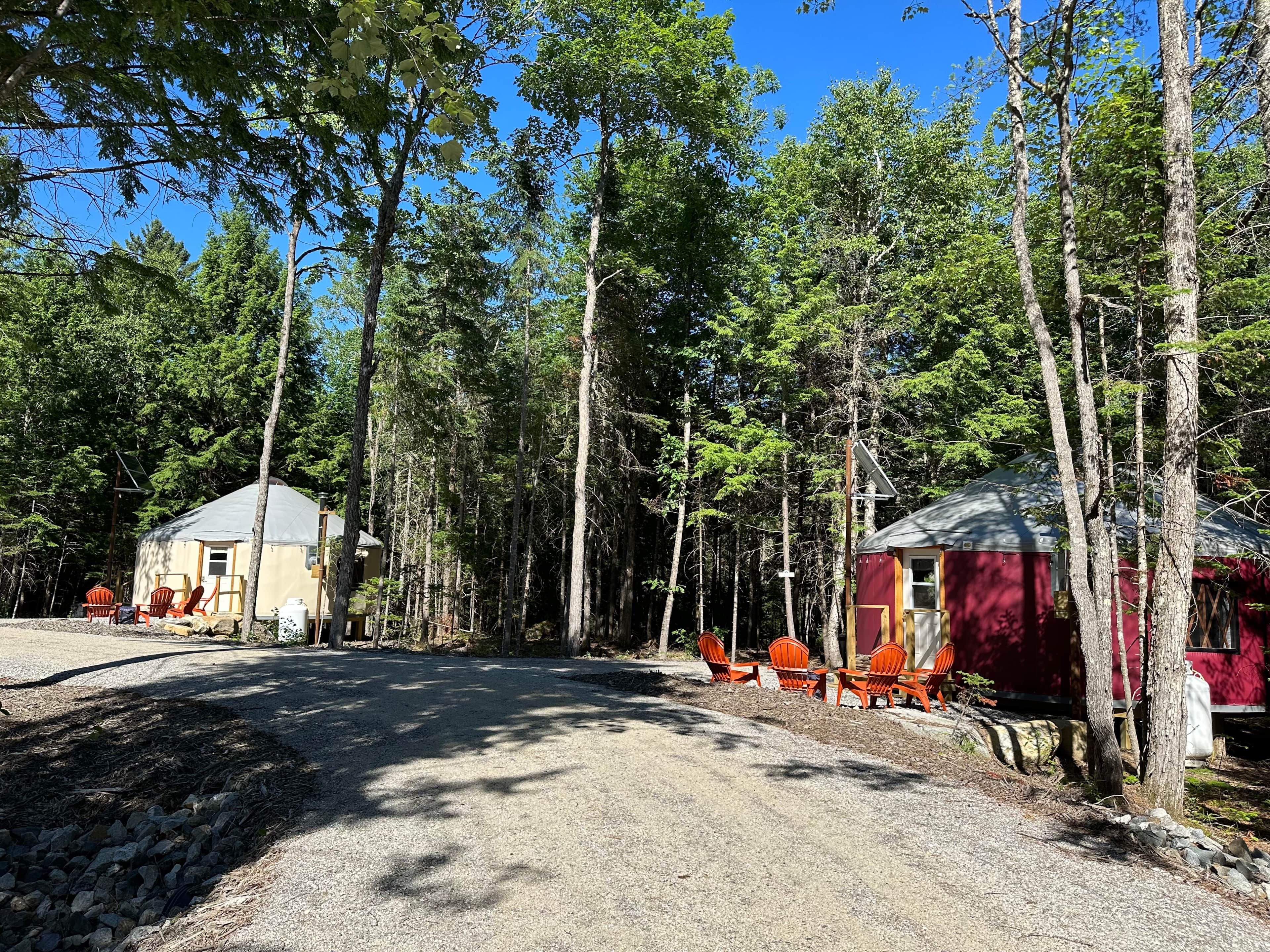 Une zone boisée comprenant deux cabanes, l’une jaune et l’autre rouge, reliées par un sentier de gravier.