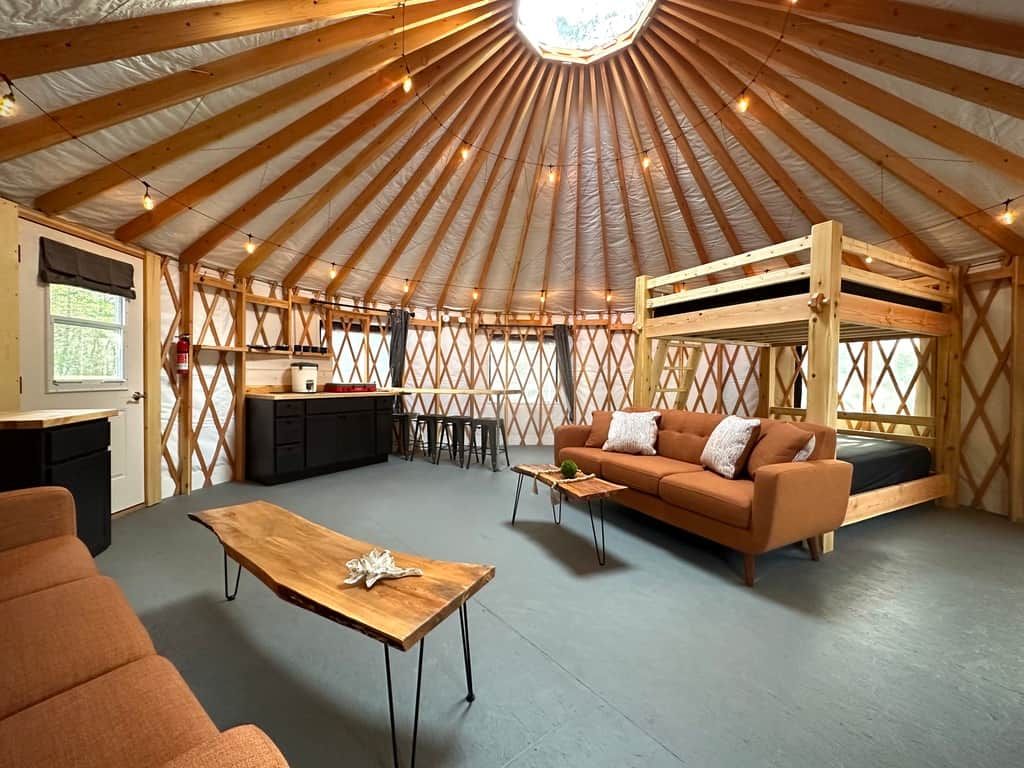 A yurt with a wooden interior, a sofa, a table, and a bunk bed.