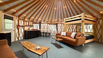 A yurt with a wooden interior, a sofa, a table, and a bunk bed.