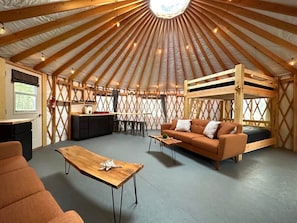 A yurt with a wooden interior, a sofa, a table, and a bunk bed.