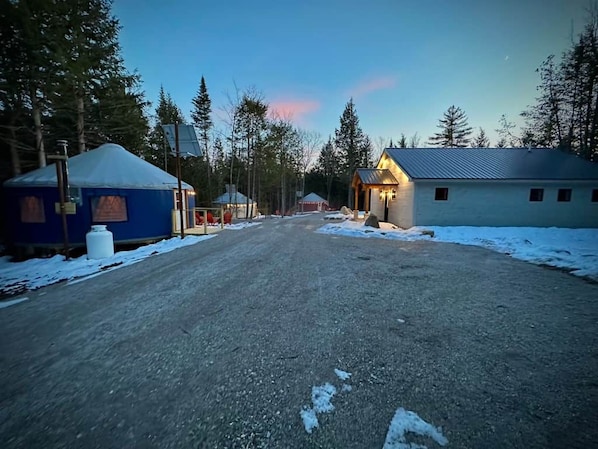 A rural road with yurts and a small building, surrounded by trees.