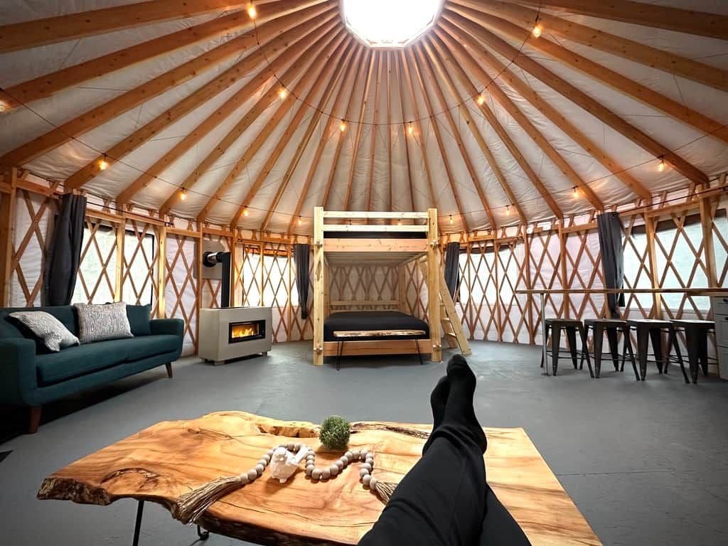 A yurt interior with a sofa, a wooden table, a bed, and a fireplace.