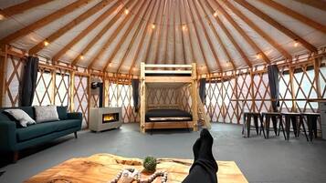 Ein Jurteninneres mit Sofa, Holztisch, Bett und Kamin.