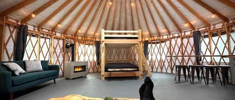 A yurt interior with a sofa, a wooden table, a bed, and a fireplace.