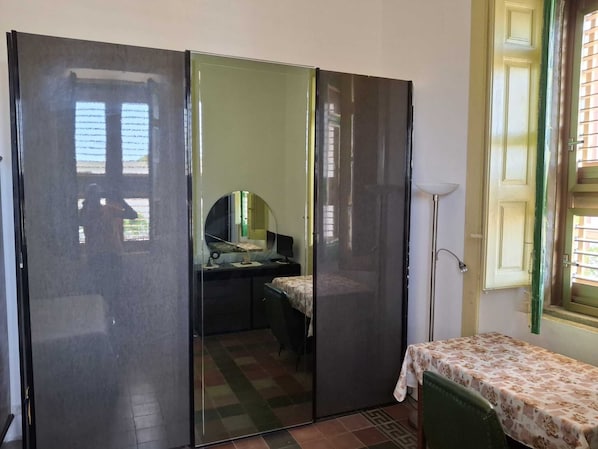 A room with a bed, a desk, a chair, a mirror, and a window with blinds.