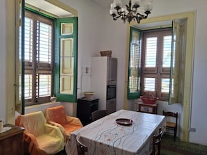 A room with a dining table, chairs, a chandelier, and windows with shutters.