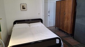 Quarto com cama, guarda-roupa e porta que dá para outro cômodo.