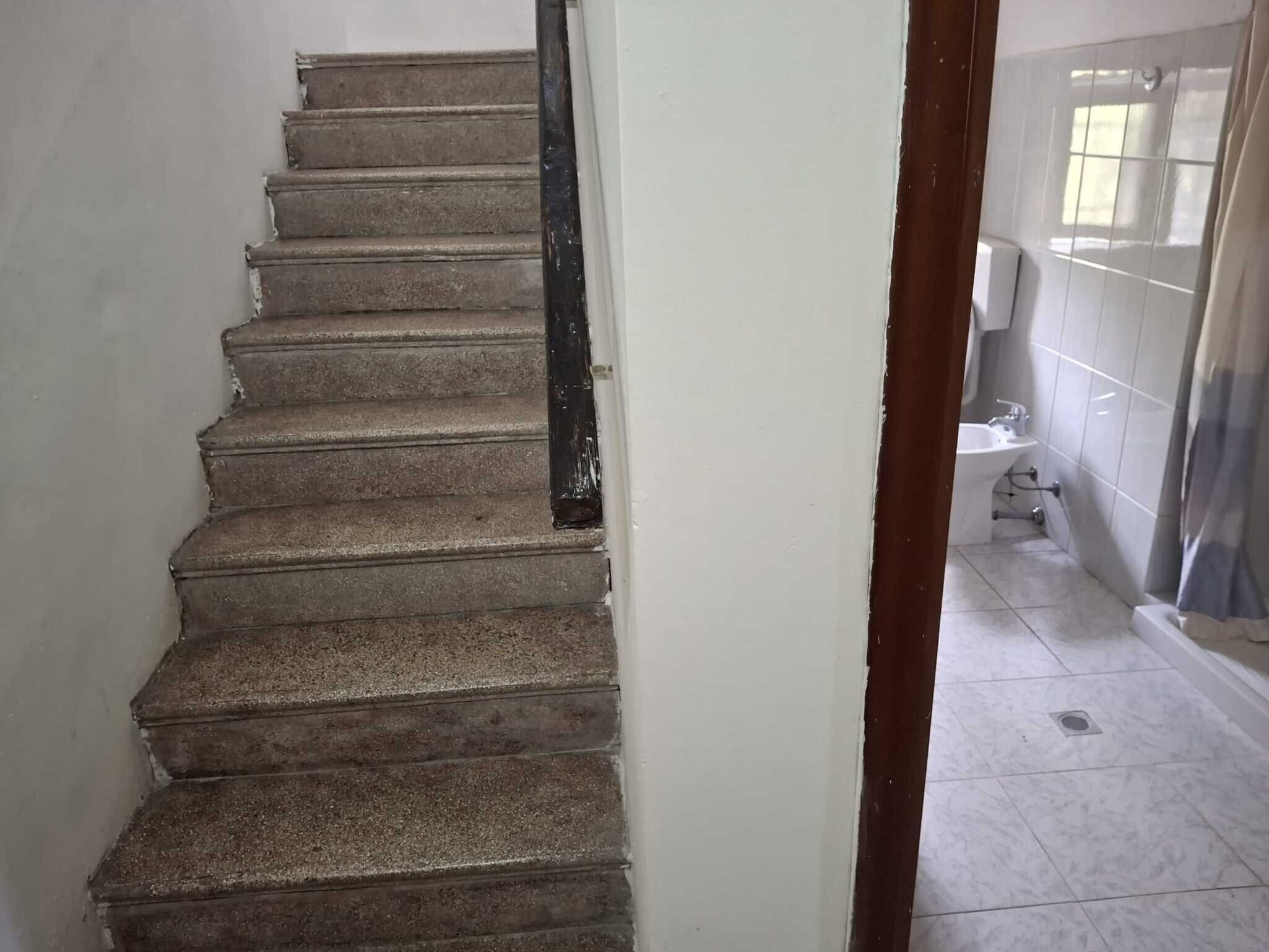 Un escalier avec une rampe noire menant à un sol carrelé.