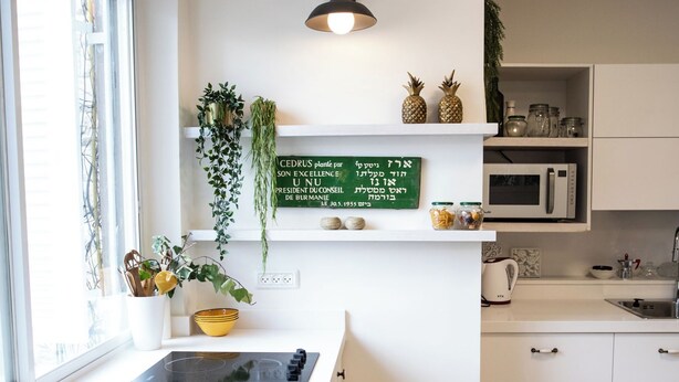 Et moderne køkken med hvide skabe, en sort induktionskogetop og et hængende, grønt skilt med hebraisk tekst.
