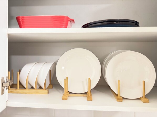 A kitchen shelf with white plates and a red bowl.