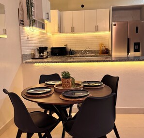 A modern kitchen with white cabinets, a central island with a sink, and a dining area with a round table and chairs.