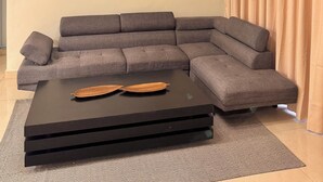 A living room with a sectional sofa, a black coffee table, decorative wall art, and a ceiling light fixture. - 3-Bedroom Apartment 20 Minutes from AILA and the Colonial District (Santo Domingo Este)