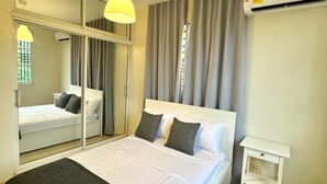 A hotel room with a bed, a bedside table, a mirror, an air conditioning unit, and a window with curtains. - 3-Bedroom Apartment 20 Minutes from AILA and the Colonial District (Santo Domingo Este)