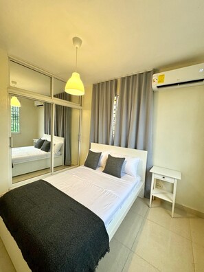 Hotelkamer met een bed, nachtkastje, spiegel, airconditioning en een raam met gordijnen.