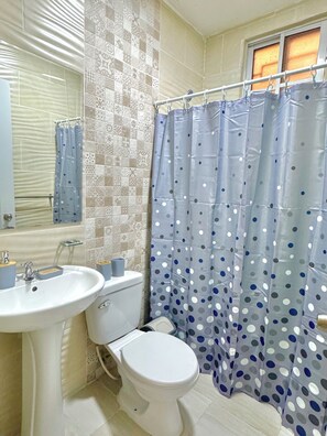 Een badkamer met een witte wastafel, toilet en douchegordijn met stippen.