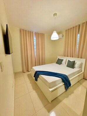 A bedroom with a bed, curtains, a hanging light fixture, and a wall-mounted air conditioner.