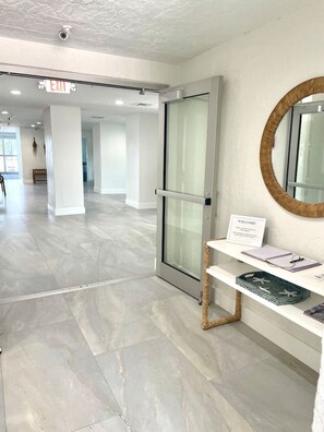 A modern interior with a glass door entrance, a welcome sign, and a bench with a basket. - One Bedroom Condo with amazing Bayviews #504 (Fort Myers Beach)