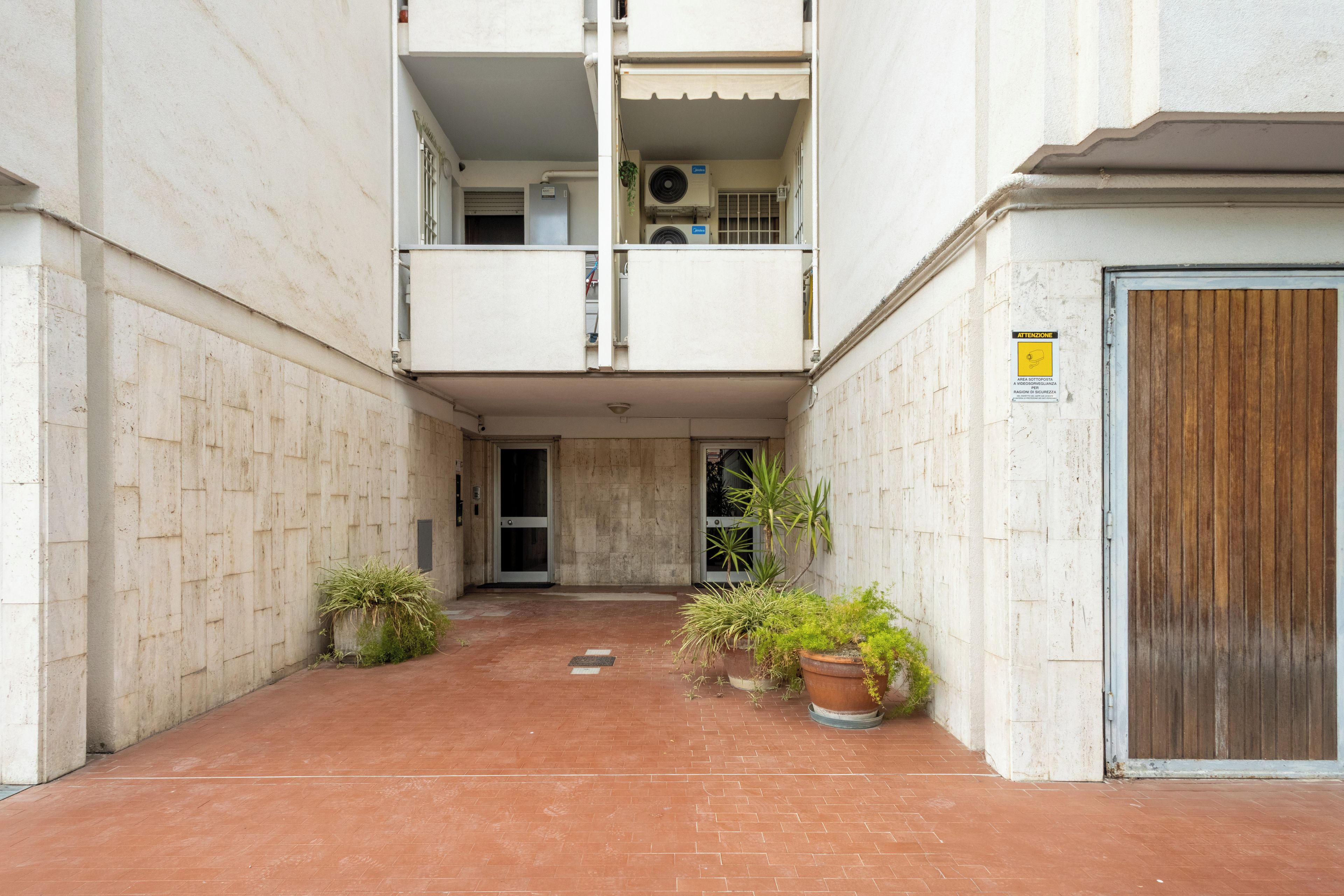 A narrow alleyway with a building entrance, potted plants, and a wooden door.