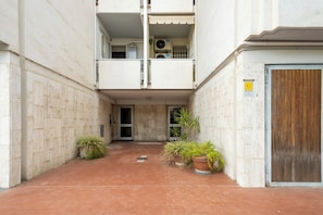 Un callejón estrecho con la entrada de un edificio, plantas en macetas y una puerta de madera.