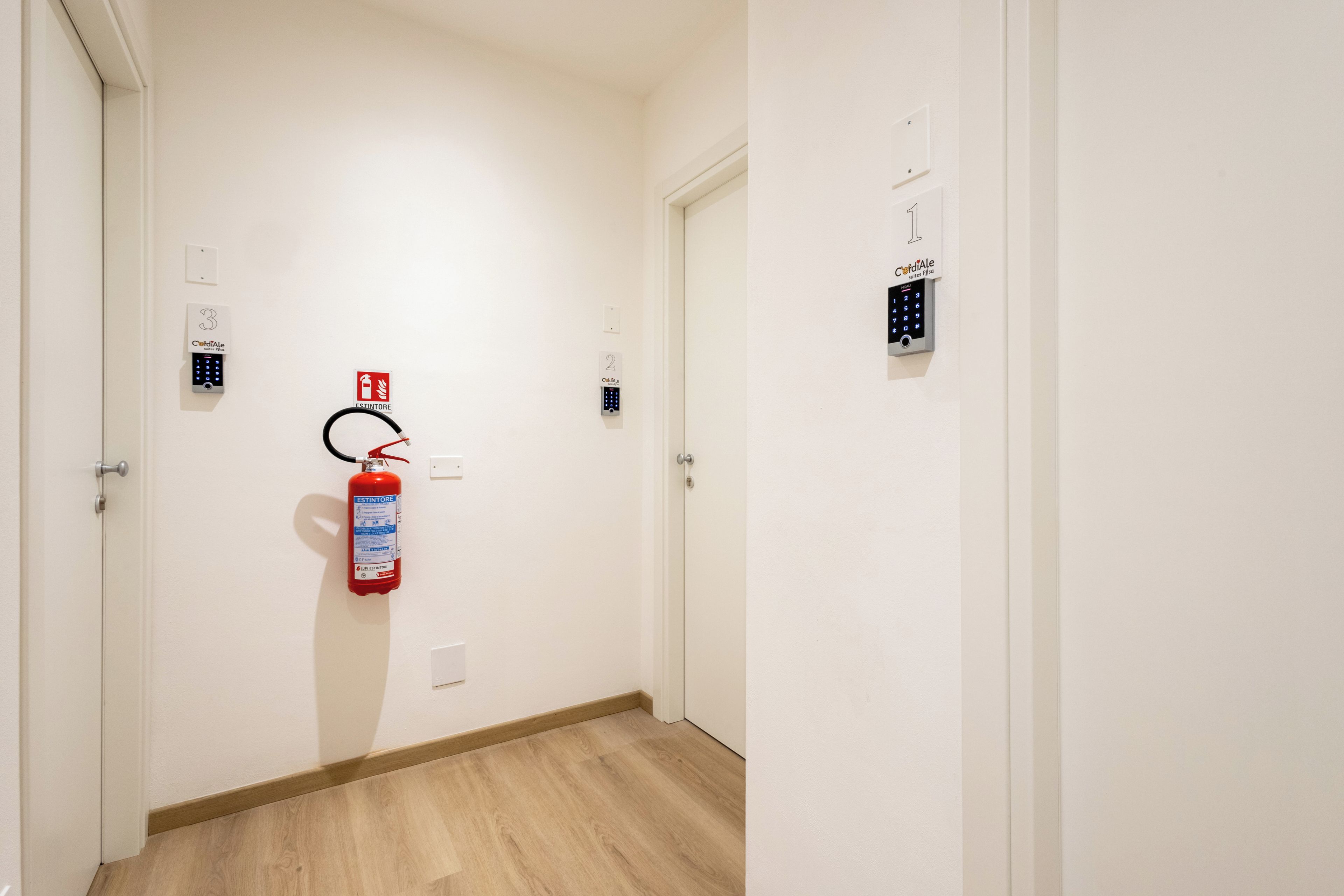 A hallway with a fire extinguisher mounted on the wall, a door with a number plate, and a keypad lock on the door.