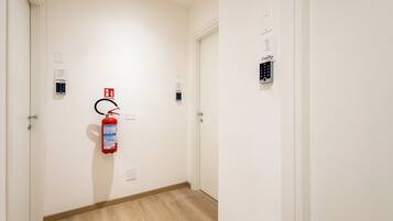 A hallway with a fire extinguisher mounted on the wall, a door with a number plate, and a keypad lock on the door.