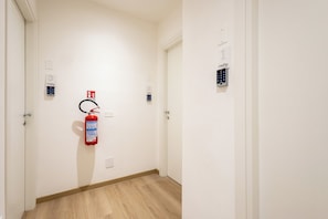 A hallway with a fire extinguisher mounted on the wall, a door with a number plate, and a keypad lock on the door. - CordiAle Suites Pisa (Pisa)