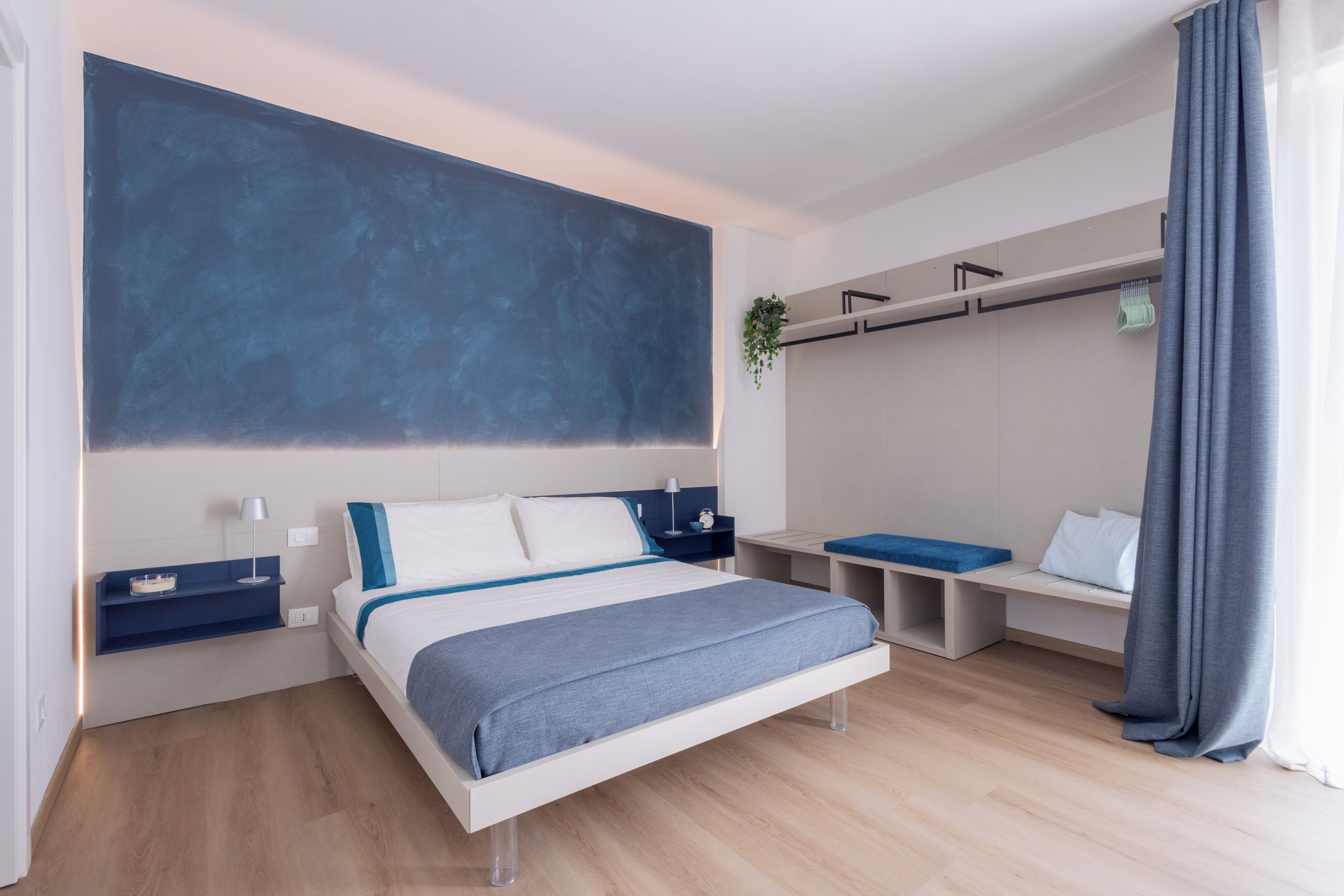 A modern bedroom with a bed, bedside tables, a desk, and a hanging plant.