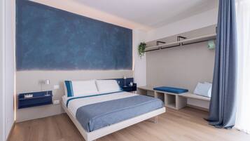 A modern bedroom with a bed, bedside tables, a desk, and a hanging plant.