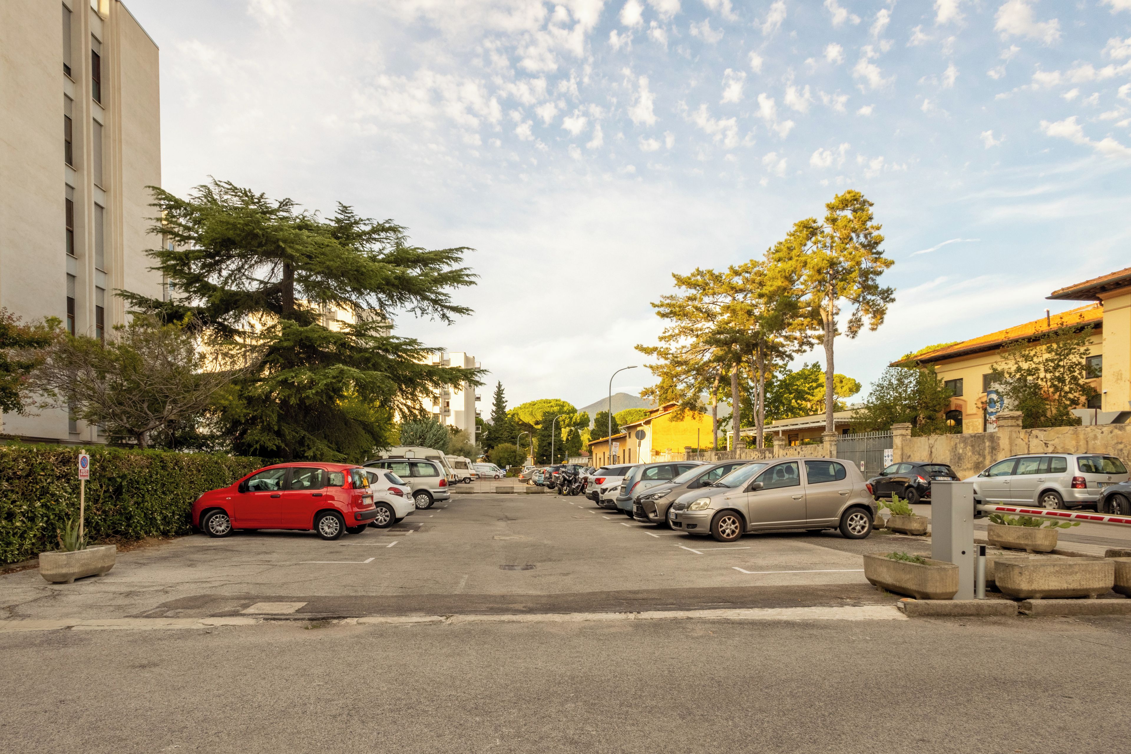 Un parking où de nombreuses voitures sont garées en rangées, entouré de bâtiments et d’arbres.