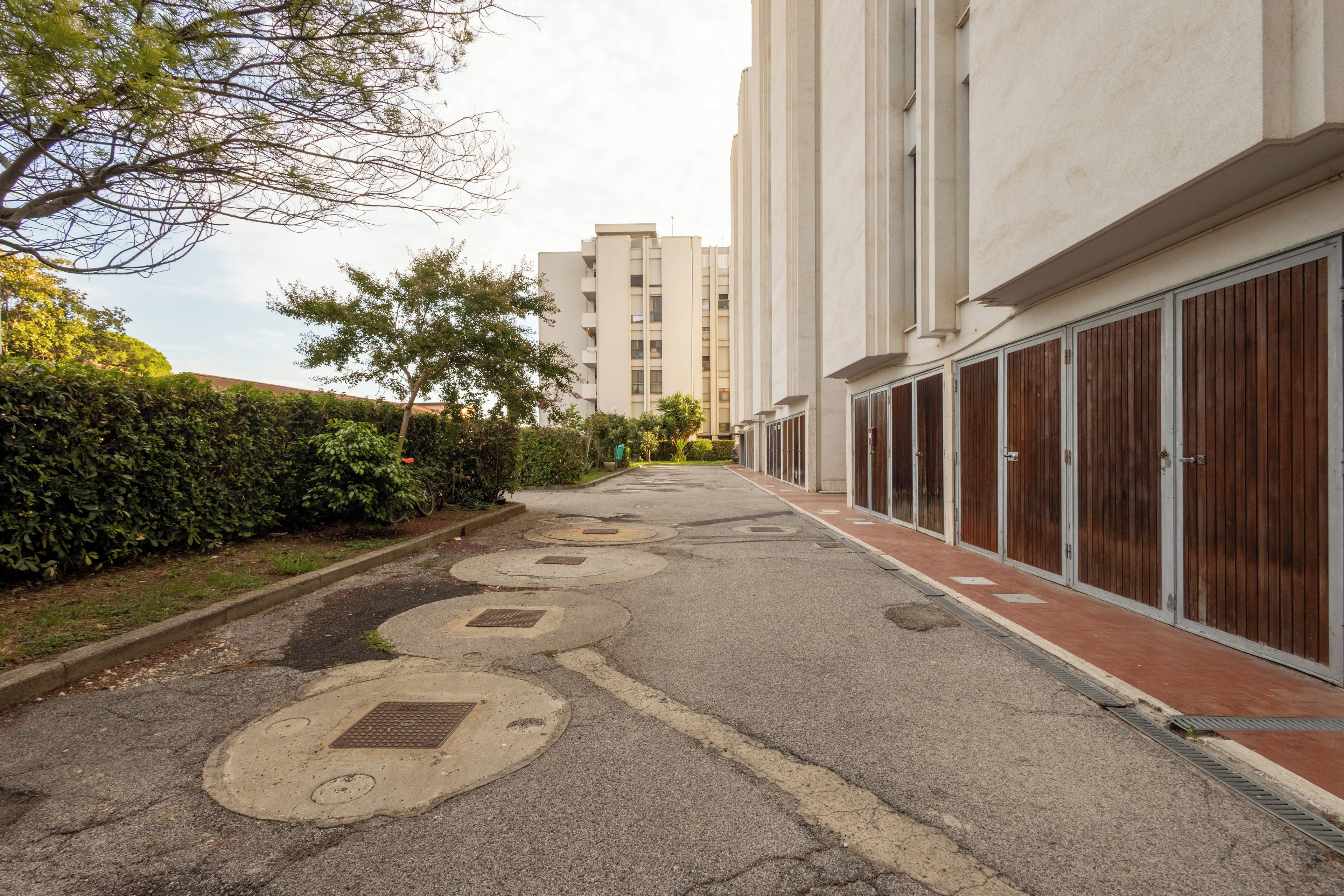 Une rue résidentielle bordée d’immeubles d’appartements, avec un trottoir et une haie.