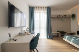 Una moderna camera d'albergo con TV a schermo piatto, una scrivania con sedia, un letto e un'ampia finestra con tende.