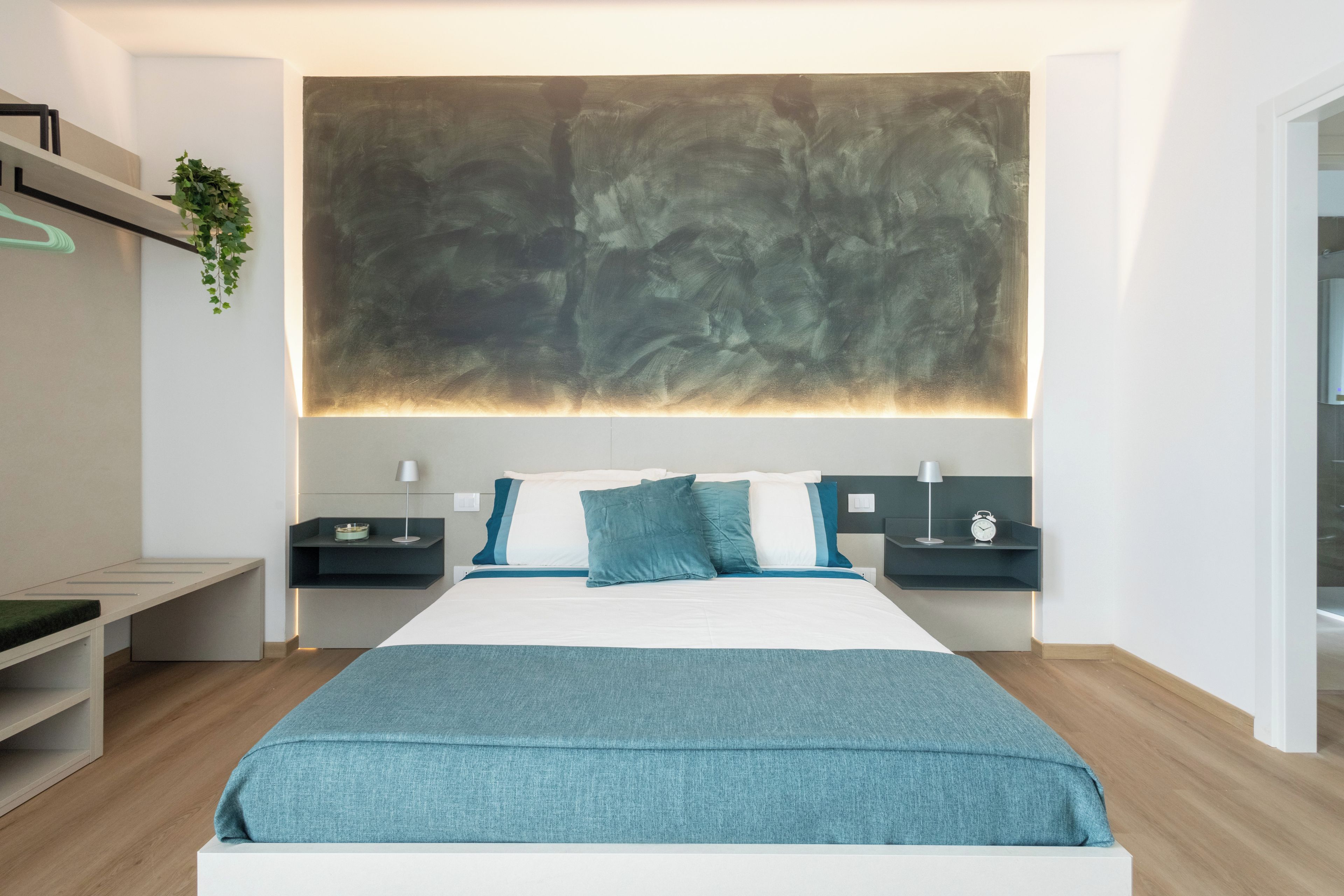 Une chambre à coucher moderne avec un grand lit, des tables de chevet, une plante suspendue et un grand tableau abstrait accroché au mur.