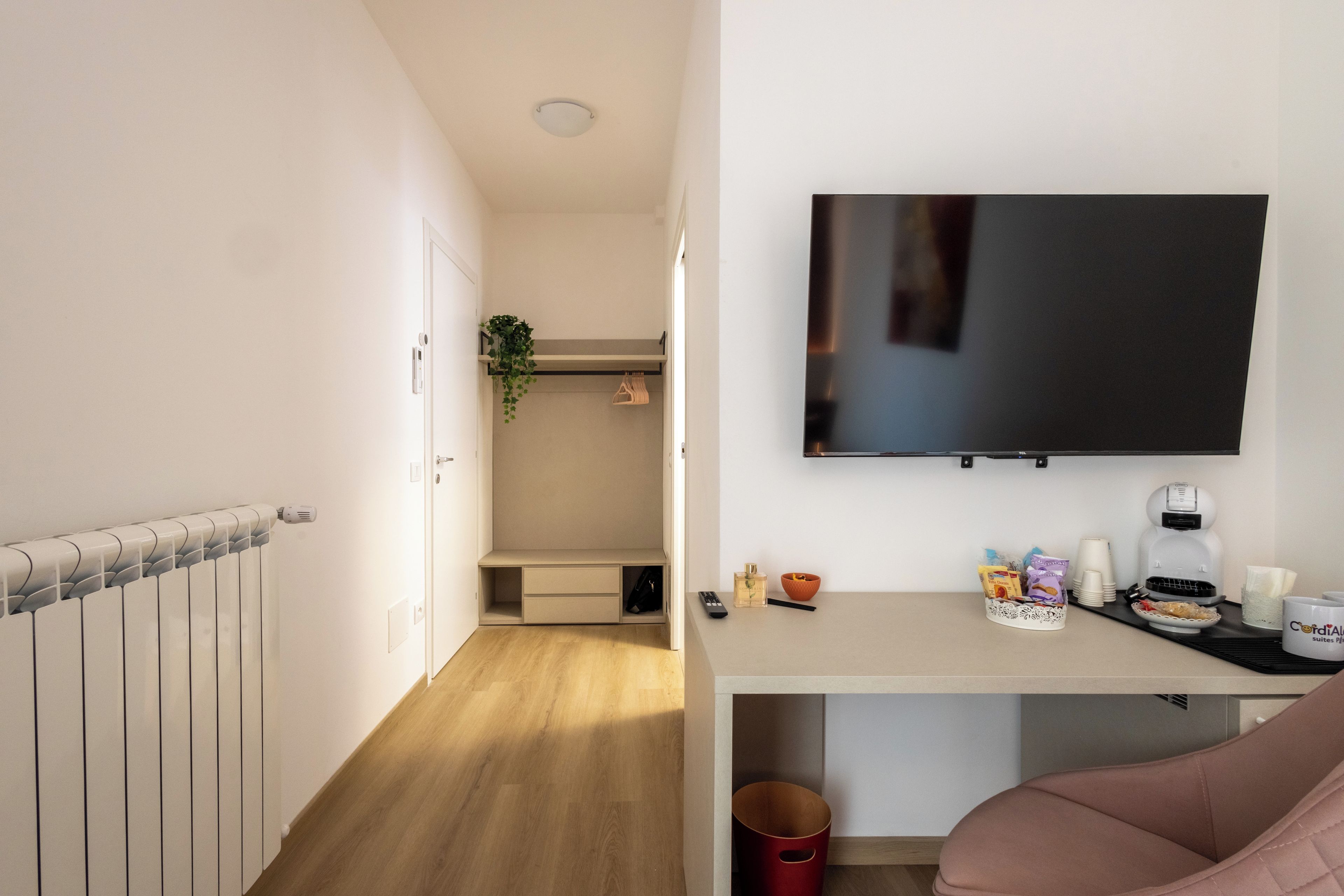 Ein Hotelzimmer mit einem Bett, einem an der Wand montierten Fernseher, einem Schreibtisch mit Kaffeemaschine und einer kleinen Pflanze.