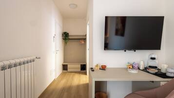 Ein Hotelzimmer mit einem Bett, einem an der Wand montierten Fernseher, einem Schreibtisch mit Kaffeemaschine und einer kleinen Pflanze.