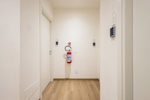 Un pasillo con un extintor montado en la pared, una puerta al final y un teclado de acceso en la pared derecha.