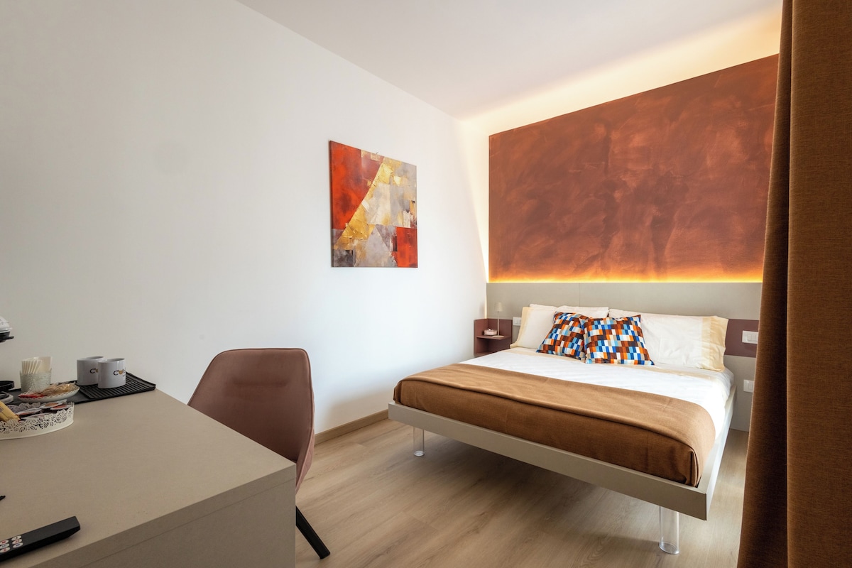 A modern hotel room with a bed, a desk, and a chair.