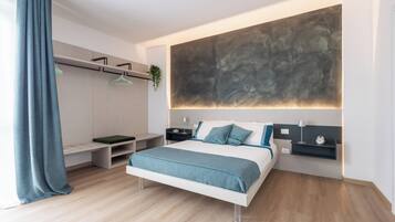 A modern bedroom with a bed, bedside tables, a wall-mounted abstract art piece, and a hanging plant.