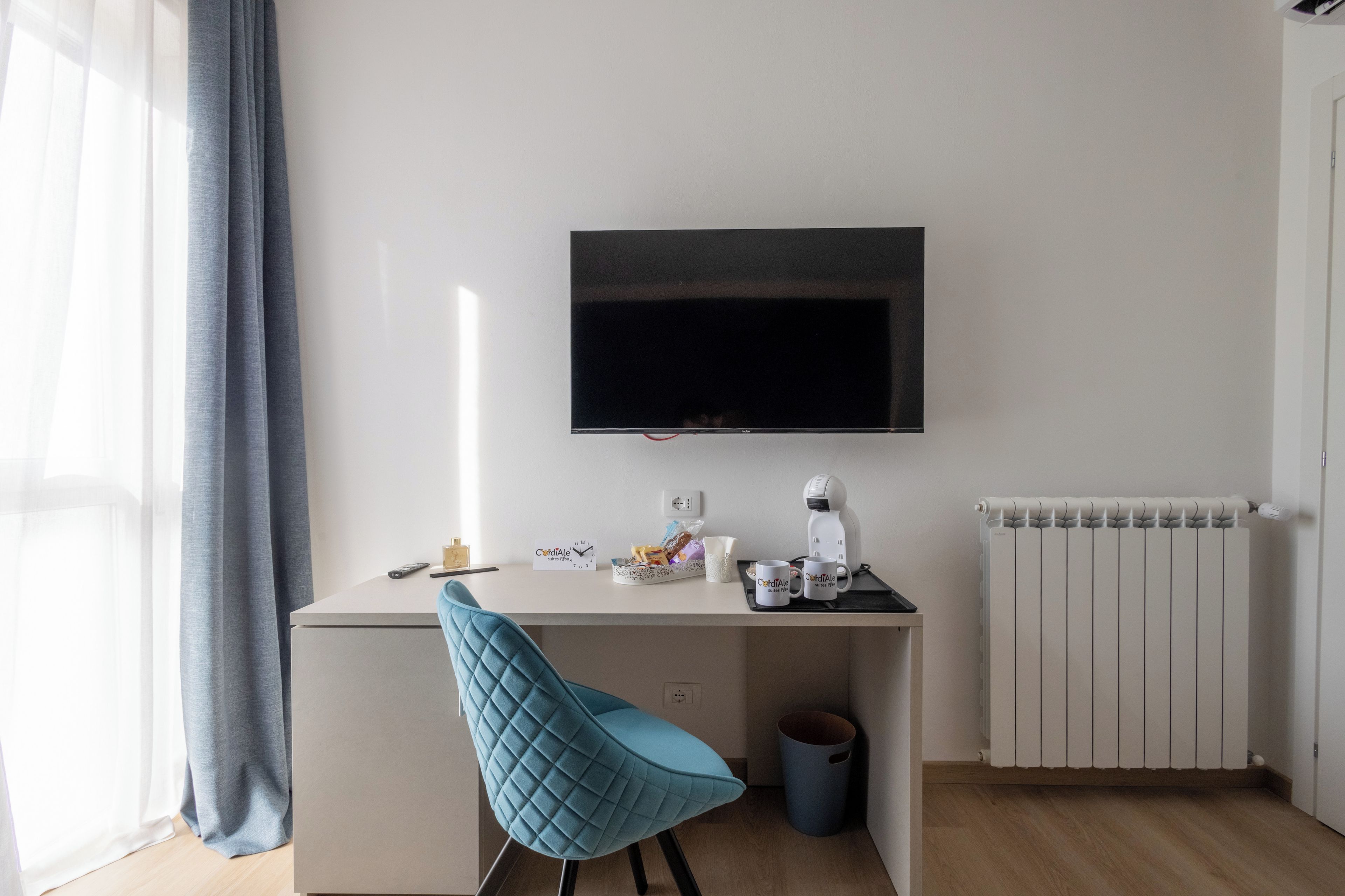 A modern, minimalistic room with a desk, a flat-screen TV, a coffee maker, and a radiator.