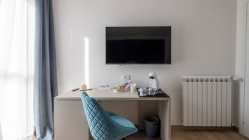 A modern, minimalistic room with a desk, a flat-screen TV, a coffee maker, and a radiator.