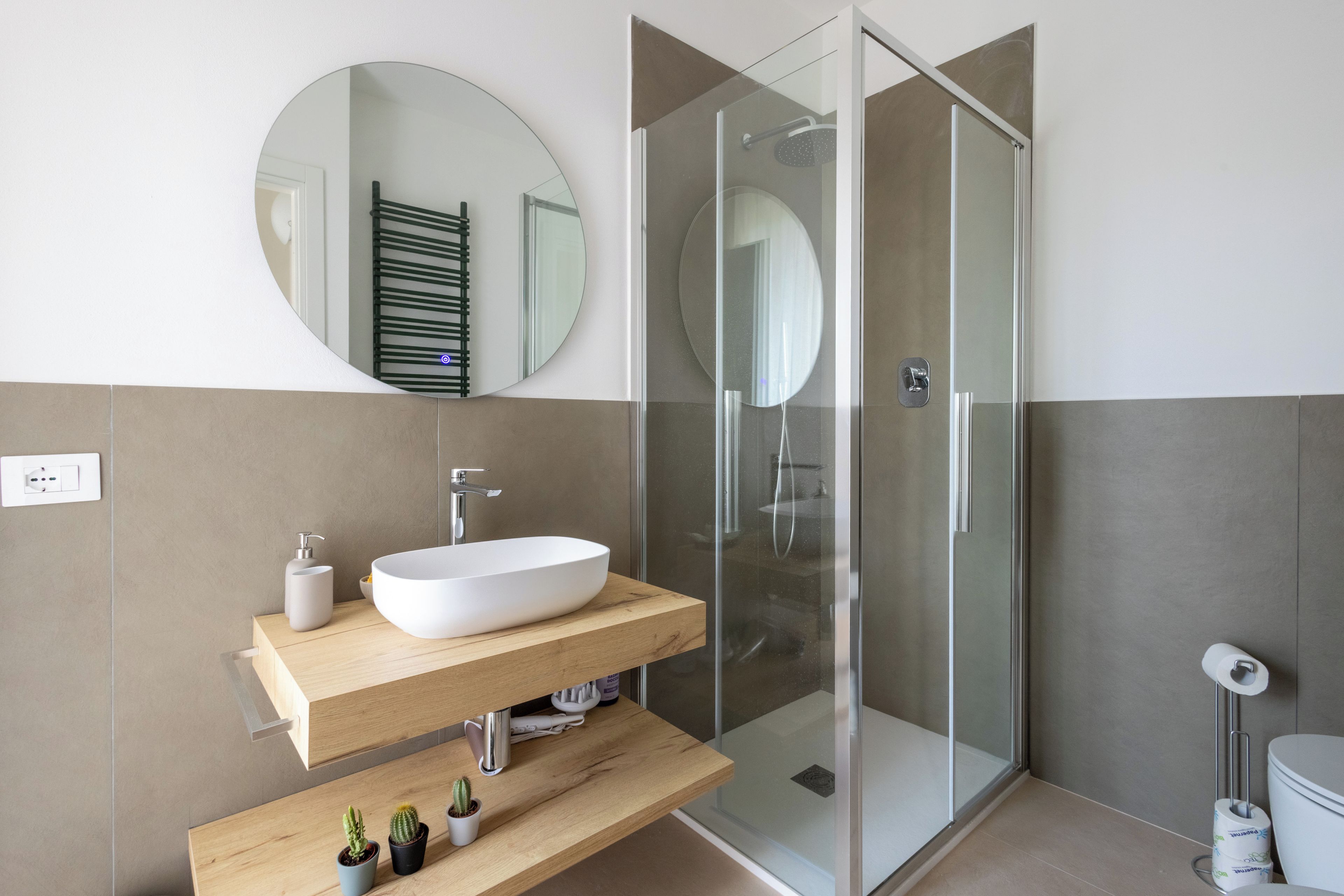 A modern bathroom with a freestanding sink, a glass shower enclosure, and a round mirror on the wall.